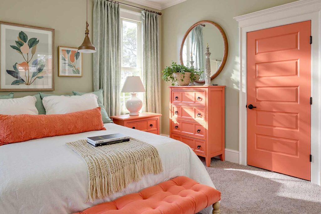 bedroom with coral door soft sage walls with cream trim and coral door and dresser, serene bedroom with a coral door painted to match a dresser in the room with soft sage walls and gray carpeting in a Phoenix Arcadia home featuring matching bench and dramatic moody lighting, painting interior doors, door painting ideas, interior door painting, interior color scheme, interior house colors, interior color pairings, painting inside doors, painting indoor doors, painting doors inside the house, interior door makeover, updating interior doors with paint