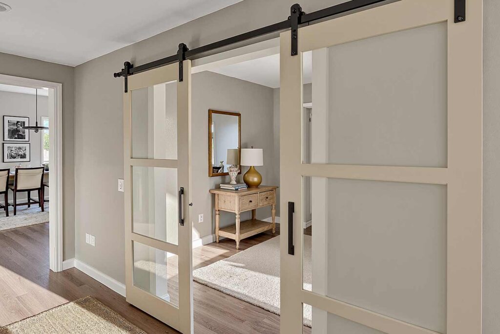 hallway with light beige barn door and cream trim and taupe walls wood floors, sophisticated hallway with a light beige barn doors cream trim and light oak flooring in a scottsdale home featuring elegant décor and dramatic moody lighting, refresh interior doors, creative door painting, door color ideas, painted door inspiration, unique door painting designs, ideas for painting doors, painting indoor doors, painting doors inside, painting home interior doors, how to paint interior doors, home color palette