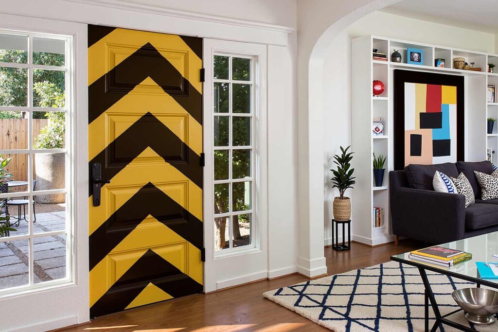 living room with graphic chevron door white walls trim wood floors, modern living room with a bold chevron-patterned door white walls walnut floors and dramatic sunlight in a scottsdale home featuring vibrant décor and moody lighting, refresh interior doors, creative door painting, door color ideas, painted door inspiration, unique door painting designs, ideas for painting doors, painting indoor doors, painting doors inside, painting home interior doors, how to paint interior doors, home color palette