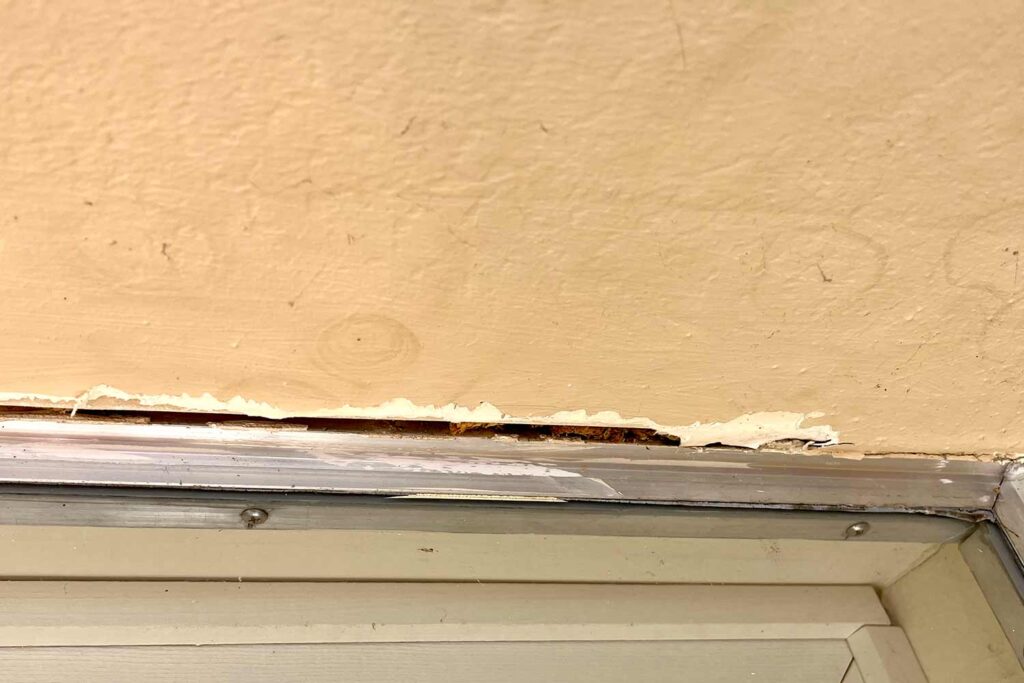 Peeling Paint and Gaps Above Window, Peeling paint and visible gaps above this window frame are clear exterior paint problems. Does my house need to be painted? Damaged paint lets moisture seep in, leading to wood rot and costly repairs. Early signs like this mean it’s time to consider exterior house painting to protect your home, , repainting exterior walls, signs your house needs painting, signs it’s time to paint your house, how to tell your house needs painting, when to repaint your house, indications your house needs new paint, clues your home needs painting, why does my house look dirty even after cleaning