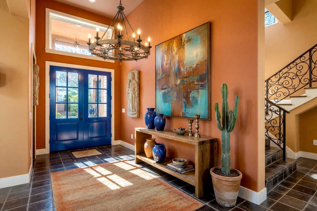 Desert Modern Foyer with Warm Terracotta Walls and Lacquered Cobalt Door-1, desert modern foyer featuring warm terracotta walls lacquered cobalt door creamy off-white trim and dusty clay ceiling in a freshly painted Scottsdale neighborhood home. natural decor includes wood console ceramic vases brass candleholder and a textured area rug illuminated by strong morning sunlight casting sharp shadows and bright highlights for a warm and striking entrance, moody color, accent wall, accent ceiling, painted ceiling, tone-on-tone, bold color contrast, color palette, coordinating colors