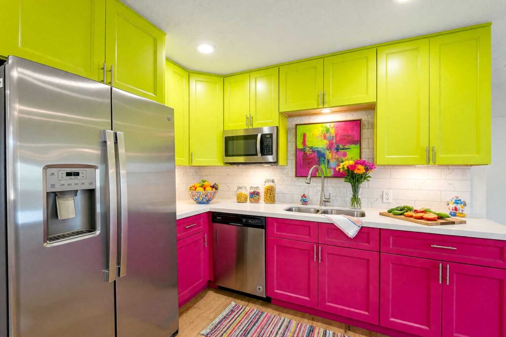 Kitchen with Electric Lime and Vivid Magenta Two-Toned Cabinets-2, a spectacular scottsdale neighborhood kitchen with shaker-style cabinets. the upper cabinets are painted in electric lime, while the lower cabinets are vivid magenta. the space features crisp white walls, bright white trim, and natural oak flooring. décor includes a colorful ceramic fruit bowl, glass jars of pasta, bright flowers, and abstract artwork. dramatic sunlight and moody lighting enhance the bold and inviting atmosphere, two-tone kitchen cabinets, dual-tone kitchen cabinets, two-color kitchen cabinets, contrasting kitchen cabinets, multi-colored kitchen cabinets