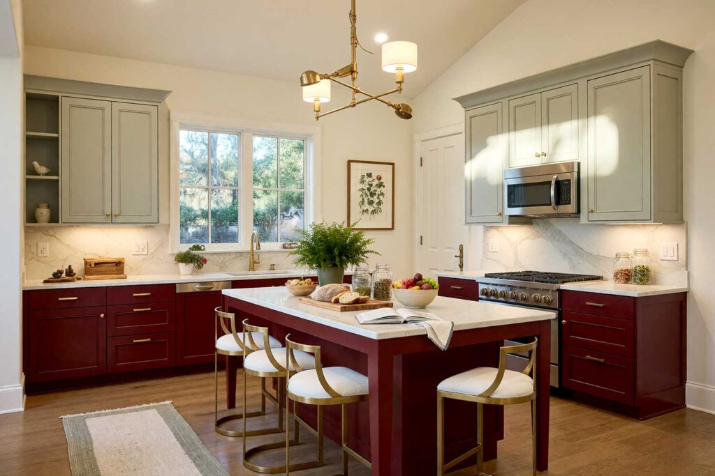 Kitchen with Oxblood Red and Pale Sage Mist Two-Toned Cabinets-1, a stunning scottsdale neighborhood kitchen with shaker-style cabinets painted in oxblood red and pale sage mist. warm cream walls and pale ivory ceiling complement antique white trim and natural oak flooring. décor includes a wooden cutting board, ceramic fruit bowl, potted plants, and botanical artwork. dramatic sunlight and moody lighting enhance the fresh and inviting atmosphere, two-tone kitchen cabinets, dual-tone kitchen cabinets, two-color kitchen cabinets, contrasting kitchen cabinets, multi-colored kitchen cabinets