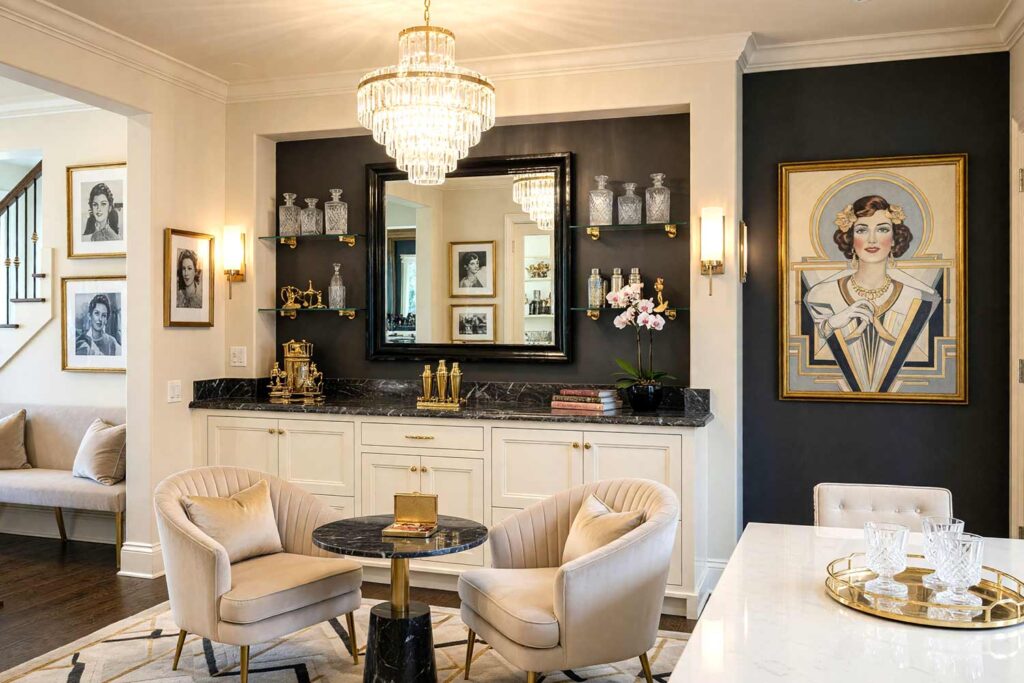 Art Deco Home Bar with Champagne Beige Walls Graphite Accent Wall and Buttercream Cabinetry-5, glamorous art deco home bar champagne beige walls graphite accent wall buttercream cabinetry bright white trim. A sophisticated home bar in a Scottsdale neighborhood featuring a black lacquered bar, buttercream velvet stools, and a dramatic sunburst mirror. Décor includes fluted glass shelves with etched crystal decanters, a crystal chandelier, and vintage Hollywood portraits. Dramatic lighting highlights the bold Art Deco palette and luxurious textures. home bar paint colors, house paint colors, paint color inspiration, bar nook colors, wet bar paint colors, cocktail nook color palette, entertainment nook paint scheme