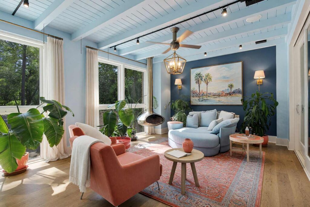 Boutique Hotel Style Sunroom with Pale Sky Blue Walls and Dark Blue Accent Wall-1, boutique hotel style sunroom pale sky blue walls dark sky blue accent wall linen white trim light oak floors mid-century modern scottsdale neighborhood. A luxurious sunroom in a Scottsdale neighborhood featuring pale sky blue walls and ceiling with a dark sky blue accent wall behind a linen white rattan bar cart. The space includes a dusty coral velvet lounge chair, a pale blue sofa, and brass lighting fixtures. Bright afternoon sunlight creates dramatic shadows and highlights, evoking a boutique hotel retreat perfect for relaxation and work. sunroom paint colors, arizona room color scheme, sunroom color scheme, sunroom color palette, sunroom colors, arizona room paint colors, arizona room paint scheme, sunroom paint ideas