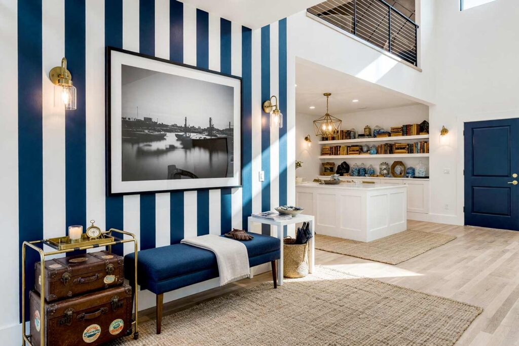 Entry Way with Navy Blue and Crisp White Striped Accent Wall-3, boutique hotel cabana entry way navy blue crisp white striped accent wall cloud white walls ceiling navy blue door. A stylish Scottsdale neighborhood entryway featuring a navy blue and crisp white striped accent wall, a navy blue door, brass luggage rack with vintage trunks, and a woven jute rug. The oversized black-and-white harbor photograph and driftwood candle create a welcoming boutique hotel vibe. Morning sunlight casts dramatic shadows, making everyday arrivals feel like a luxurious vacation. painting striped walls, painting wall stripes, painted wall stripes, two tone striped walls, painting striped accent walls, striped wall paint ideas, painted stripe walls