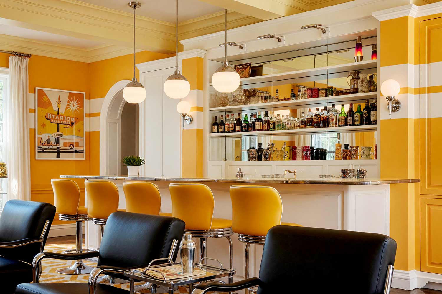 Fun Retro Atomic Home Bar with Marigold and White Striped Walls-6, fun retro atomic home bar warm marigold soft white striped walls pale yellow ceiling bright white trim. A nostalgic home bar in a Scottsdale neighborhood featuring bold marigold and white striped walls, soft white cabinetry, and chrome accents. Décor includes retro diner pop art, lava lamps, tiki mugs, and chrome pendant lighting. Dramatic natural and artificial light highlights the playful mid-century modern palette and textures of this lively space. bar cabinet paint colors, home bar color palette, wine nook paint colors, built-in bar paint scheme, bar area color combinations