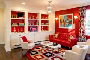 Retro Diner-Inspired Living Room with Cherry Red Accent Wall and Soft Cream Shelving-4-FEATURE, retro living room with cherry red accent wall soft cream shelving chrome trim and dark oak flooring. A vibrant 1950s-inspired living room in a Scottsdale neighborhood featuring a tufted cherry red vinyl sofa, kidney-shaped coffee table, and retro bar cart. Built-in shelving showcases vintage board games, tiki mugs, and a chrome-edged record player, while a starburst chandelier and bold geometric rug complete the nostalgic diner-style aesthetic. Bright morning sunlight casts dramatic shadows, enhancing the playful, glossy look of this charming mid-century space. Bookshelf paint color ideas, Painting built-in bookshelves, Color ideas for painting bookshelves, Built-in bookcase design ideas, Ideas for painting built-in shelves, Built-in bookshelf color inspiration, Bookcase paint colors