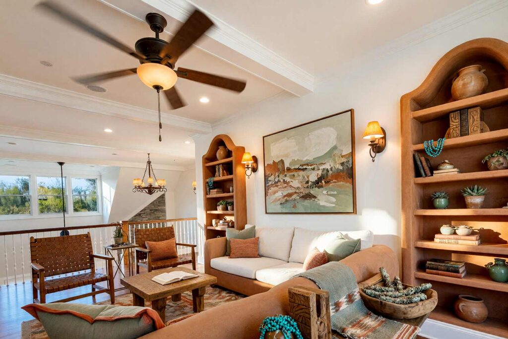Southwestern Hacienda Living Room with Terracotta Clay Shelving-3, southwestern hacienda living room terracotta clay shelving sage whisper accents bone white walls warm white ceiling. A sun-warmed living room in a Scottsdale neighborhood featuring terracotta clay built-in shelves adorned with raw clay pots, turquoise beads, and sage green ceramics. A low-profile adobe-style sofa, Navajo-patterned rug, and wrought iron chandelier complete the Southwestern aesthetic. Late afternoon sunlight highlights the textures and colors, offering grounded bookshelf paint color ideas for painting built-in bookshelves inspired by desert living. bookshelf paint color ideas, painting built-in bookshelves, color ideas for painting bookshelves, built-in bookcase design ideas, ideas for painting built-in shelves, built-in bookshelf color inspiration, bookcase paint colors