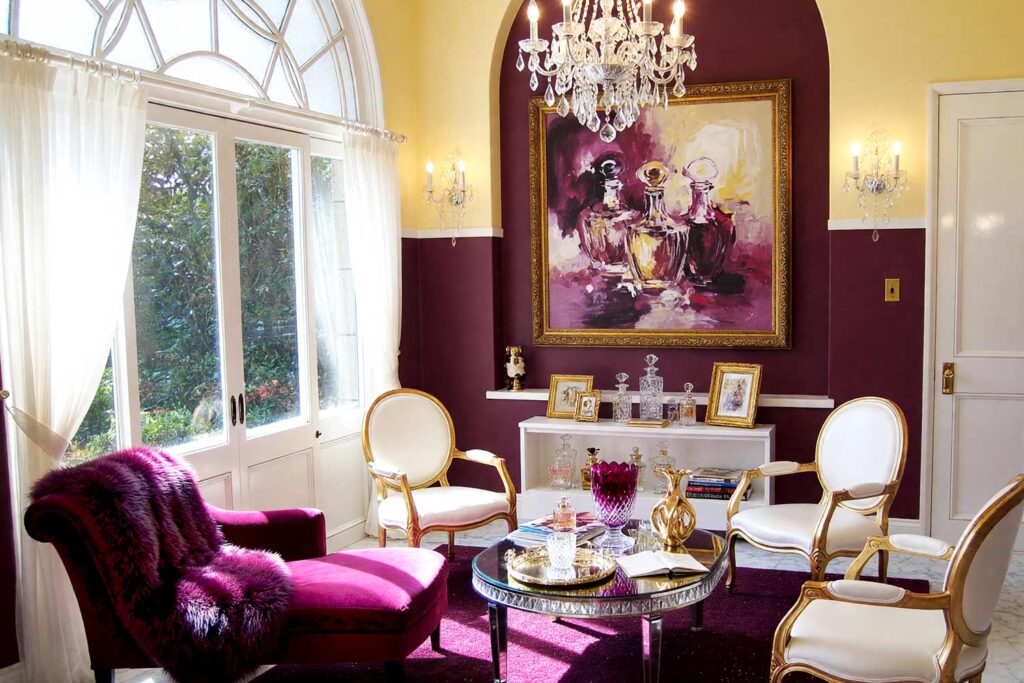 Sunroom with Pale Butter Yellow and Deep Aubergine Walls-2, glitz and glam statement sunroom pale butter yellow walls deep aubergine accent wall crisp white trim polished marble floors scottsdale neighborhood. A luxurious sunroom in a Scottsdale neighborhood featuring pale butter yellow walls and ceiling with a deep aubergine accent wall. The space includes a deep aubergine velvet chaise with a faux fur throw, a crystal-cut vase on a mirrored side table, and a sparkling crystal chandelier. Afternoon sunlight creates dramatic shadows and dazzling highlights, evoking a glamorous and indulgent retreat perfect for relaxation and entertaining. sunroom paint palette, arizona room paint palette, sunroom wall colors, sunroom paint inspiration, desert sunroom color ideas, arizona room decor colors, sun porch paint colors