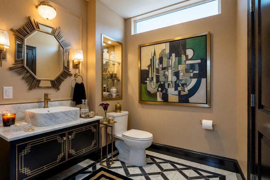 Art Deco Powder Room with Camel Walls and Deep Charcoal Vanity-4, art deco powder room neutral interior paint colors camel walls deep charcoal vanity deep charcoal trim marble tile flooring. A glamorous powder room in a Scottsdale neighborhood featuring a deep charcoal vanity, sunburst geometric mirror, fluted brass sconces, and black-and-white marble floors. Outfitted with a cubist architecture artwork, crystal-cut soap dish, and burning amber candle. High-contrast directional light generates dramatic shadows and rich, glowing metallic highlights. neutral tones for interiors, neutral wall paint colors, muted neutral colors, soft neutral color palette, interior neutral color palette