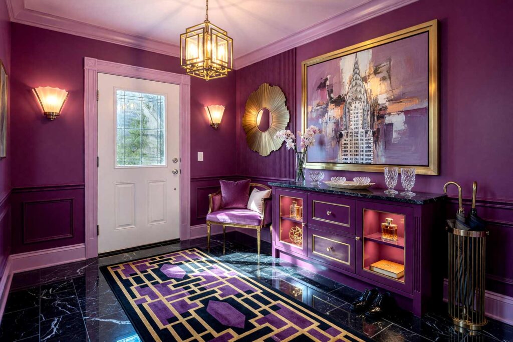 Glamorous Art Deco Entryway with Mid Plum Walls Deep and Aubergine Millwork-2, art deco entryway tone-on-tone interior paint mid plum walls lilac mist ceiling lilac mist trim deep aubergine millwork black marble flooring. A glamorous first impression in a Scottsdale neighborhood featuring mid plum walls, shiny lilac mist trim, and custom deep aubergine millwork. Outfitted with black marble floors, a fan-shaped mirror, a geometric runner rug, and a Chrysler Building abstract canvas with rose gold accents. Bright afternoon sunlight contrasts with deep shadows, creating a captivating and luxurious space. tone-on-tone interior paint, monochromatic paint scheme, tonal palette, layered look, value variations, monochromatic color scheme, tone-on-tone painting technique, single-color paint scheme