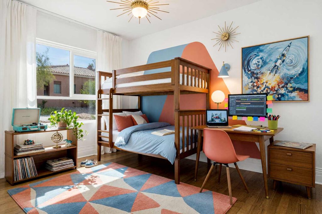 Atomic Bunk Room Child’s Bedroom with Powder Blue and Warm Coral Wall Design-6, kid’s bedroom paint colors mid-century atomic cloud white powder blue dusty coral walnut floor. An energetic Mid-Century Modern child's bunk room in a Scottsdale neighborhood featuring cloud white walls, a retro painted boomerang accent panel in powder blue and dusty coral, and lustrous cloud white semi-gloss woodwork. The design showcases a walnut bunk bed with tapered legs, a built-in record player station, and an active homework desk equipped with an illuminated dual-screen computer setup surrounded by everyday study supplies. Rich walnut flooring and dramatic, high-contrast daylight make this an inspiring space for homework and play. kids bedroom paint ideas, child's bedroom color palette, kids room paint colors, toddler bedroom paint colors, kids bedroom colors