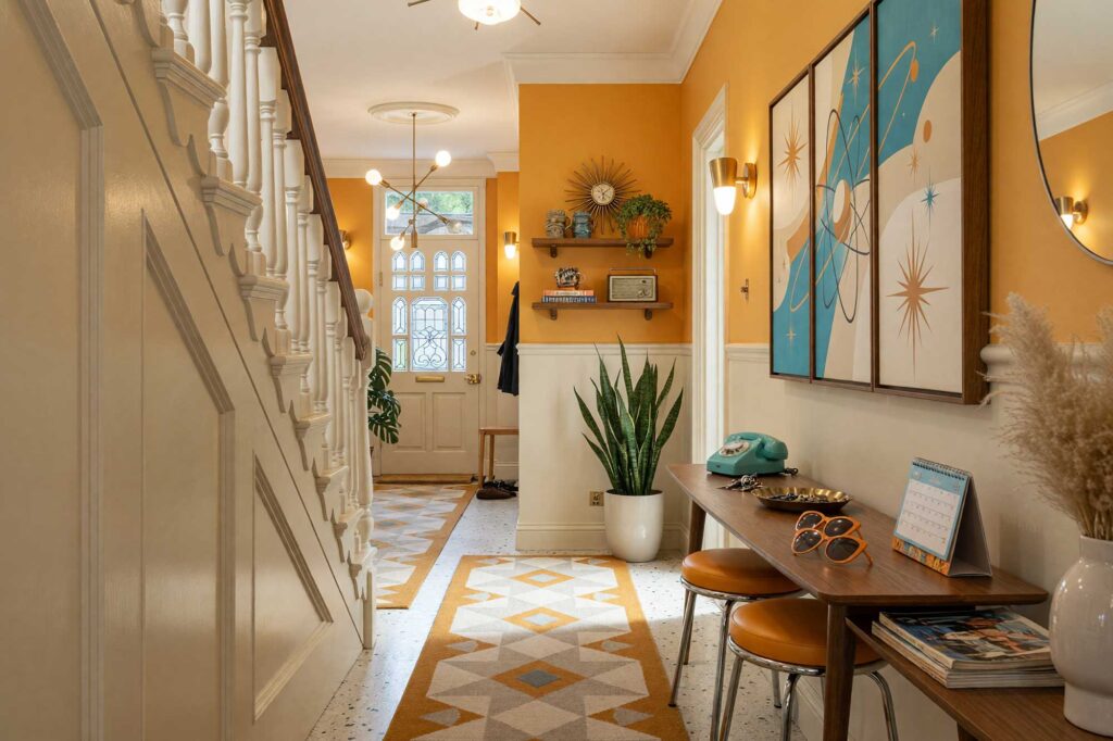 Atomic Kitsch Hallway with Pale Putty Walls and Muted Marigold Accent-1-FEATURE, kitsch themed room paint retro hallway pale putty walls muted marigold accent wall soft white ceiling cream terrazzo tile flooring. Situated in an upscale Scottsdale neighborhood, this vibrant retro corridor showcases a walnut boomerang console table, a vertical triptych atomic satellite art piece, brass cone sconces, and an eye-catching muted marigold accent wall. Baseboards and woodwork gleam with fresh semi-gloss paint, balancing playful mid-century kitsch decor like ceramic flamingos and a starburst clock against polished terrazzo flooring.
