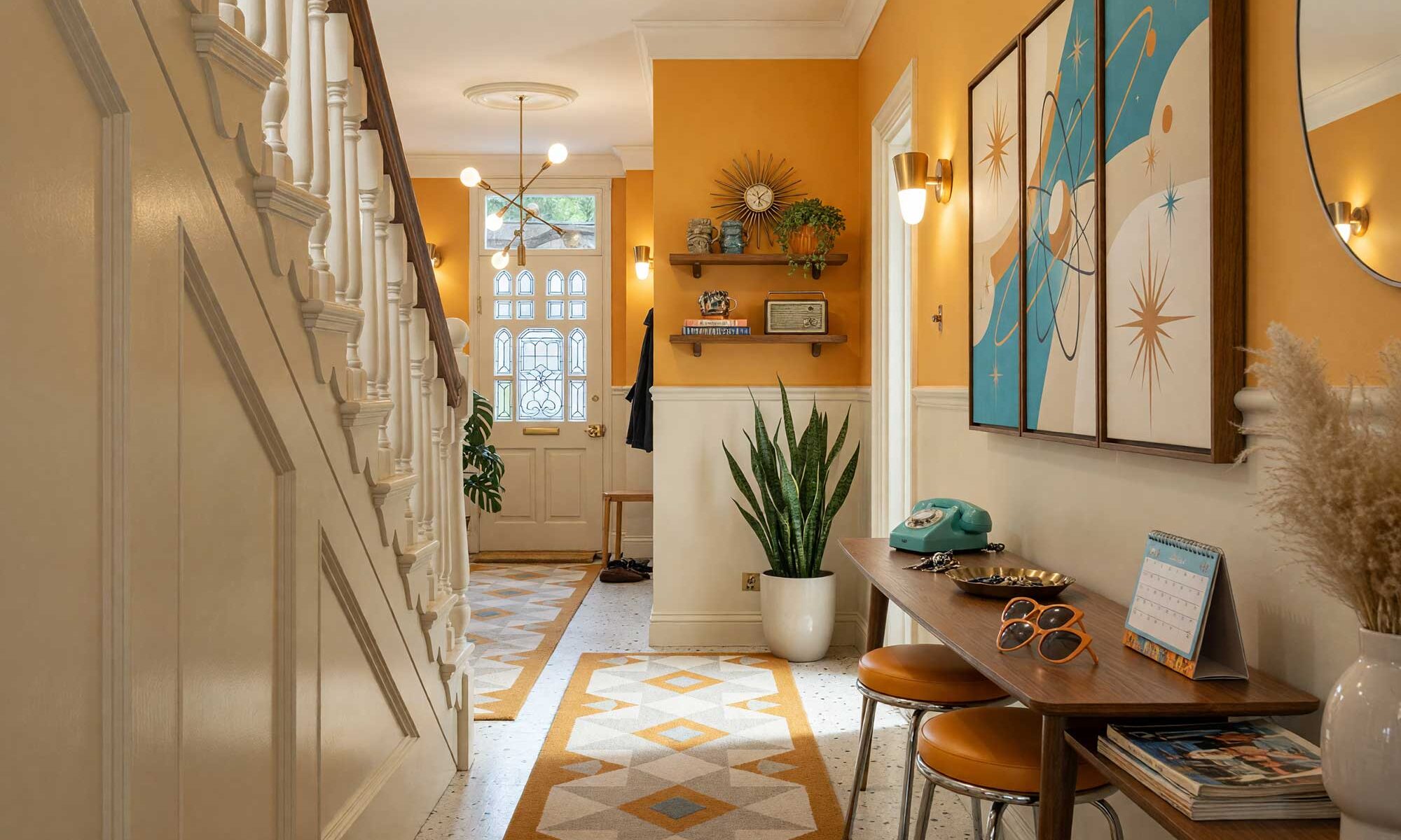 Atomic Kitsch Hallway with Pale Putty Walls and Muted Marigold Accent-1-FEATURE, kitsch themed room paint retro hallway pale putty walls muted marigold accent wall soft white ceiling cream terrazzo tile flooring. Situated in an upscale Scottsdale neighborhood, this vibrant retro corridor showcases a walnut boomerang console table, a vertical triptych atomic satellite art piece, brass cone sconces, and an eye-catching muted marigold accent wall. Baseboards and woodwork gleam with fresh semi-gloss paint, balancing playful mid-century kitsch decor like ceramic flamingos and a starburst clock against polished terrazzo flooring.