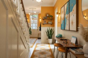 Atomic Kitsch Hallway with Pale Putty Walls and Muted Marigold Accent-1-FEATURE, kitsch themed room paint retro hallway pale putty walls muted marigold accent wall soft white ceiling cream terrazzo tile flooring. Situated in an upscale Scottsdale neighborhood, this vibrant retro corridor showcases a walnut boomerang console table, a vertical triptych atomic satellite art piece, brass cone sconces, and an eye-catching muted marigold accent wall. Baseboards and woodwork gleam with fresh semi-gloss paint, balancing playful mid-century kitsch decor like ceramic flamingos and a starburst clock against polished terrazzo flooring.