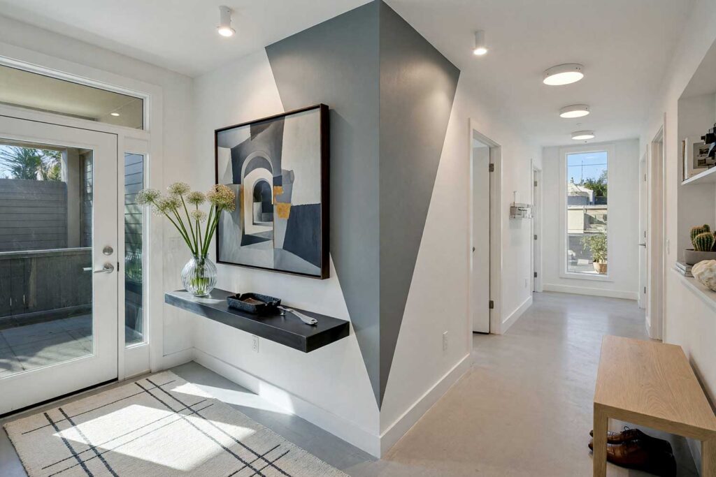 Contemporary Hallway with Light Gray Walls and Slate Gray Corner Graphic-6, contemporary hallway light gray walls darker slate gray painted wall graphics white ceiling polished concrete flooring. A dramatic corridor in a Scottsdale neighborhood featuring light gray walls, a crisp white ceiling, and an inverted triangular corner painted wall graphic in slate gray. Appointed with a floating blackened steel console, architectural artwork, and polished concrete floors. Razor-sharp natural sunlight creates deep shadows, transforming this hallway into a stunning contemporary gallery space. hand-painted wall designs, decorative wall painting
