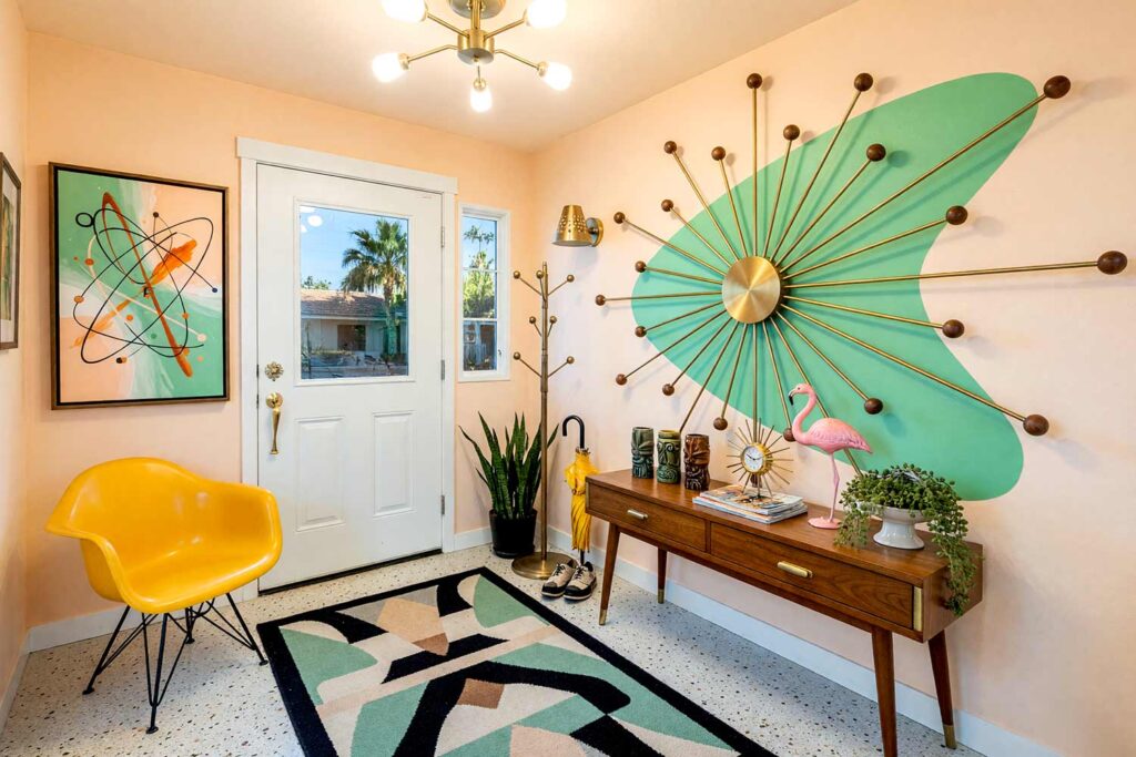 Entryway with White Walls and Retro Seafoam Boomerang Design with Radial Brass Spoke Rods-3, retro atomic entryway shell white walls retro seafoam boomerang radial brass spoke rods coconut white baseboards terrazzo floors painting creative wall treatments. A 1950s atomic foyer in a Scottsdale neighborhood featuring a tapered-leg walnut console, yellow fiberglass shell chair, terrazzo floors, and a retro seafoam painted boomerang wall accent with radial brass spokes. Afternoon sun beams through sidelights, casting dramatic starburst shadows that highlight the shiny coconut white trim and atomic kitsch entryway styling. painted accent wall with metal, dimensional accent wall, architectural accent wall, painted mural wall with metal accents, unique accent wall ideas, textured painted walls