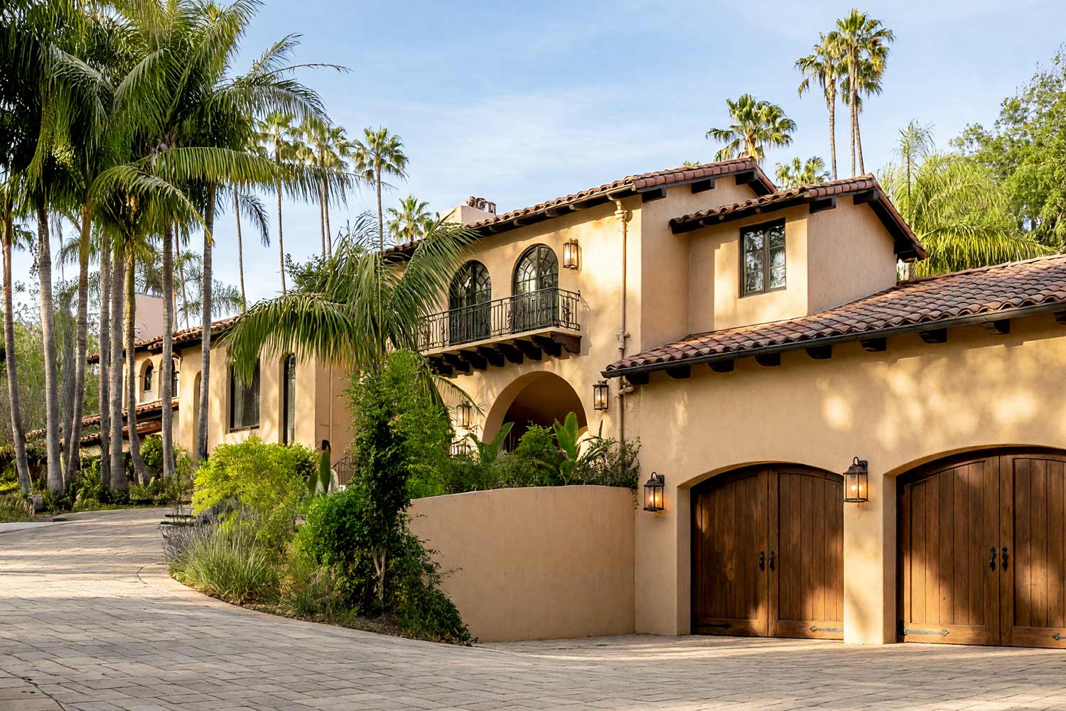 Hillside Spanish Revival with Sand Stucco and Burnt Umber Trim-2, Desert sand stucco and burnt umber trim bring warm Sedona Spanish Revival character to this hillside villa, framed by flamed terracotta roof tile and stone pavers. southwestern spanish revival exterior paint colors desert sand stucco burnt umber canecillos flamed terracotta roof tiles stone paver driveway front facade. A tailored Arizona villa in Scottsdale featuring authentic mineral stucco, glossy hand-finished trim, and rich curb appeal. A burnt umber door and weathered russet ironwork contrast warm desert sand stucco and flamed terracotta roofing. Realistic landscaping with subtle natural debris, active brass sprinklers, patterned textiles, and golden hour lighting complete this Sedona-inspired desert exterior. santa barbara style paint colors, spanish hacienda exterior paint colors, mediterranean revival exterior colors, stucco house paint colors, terracotta roof house colors