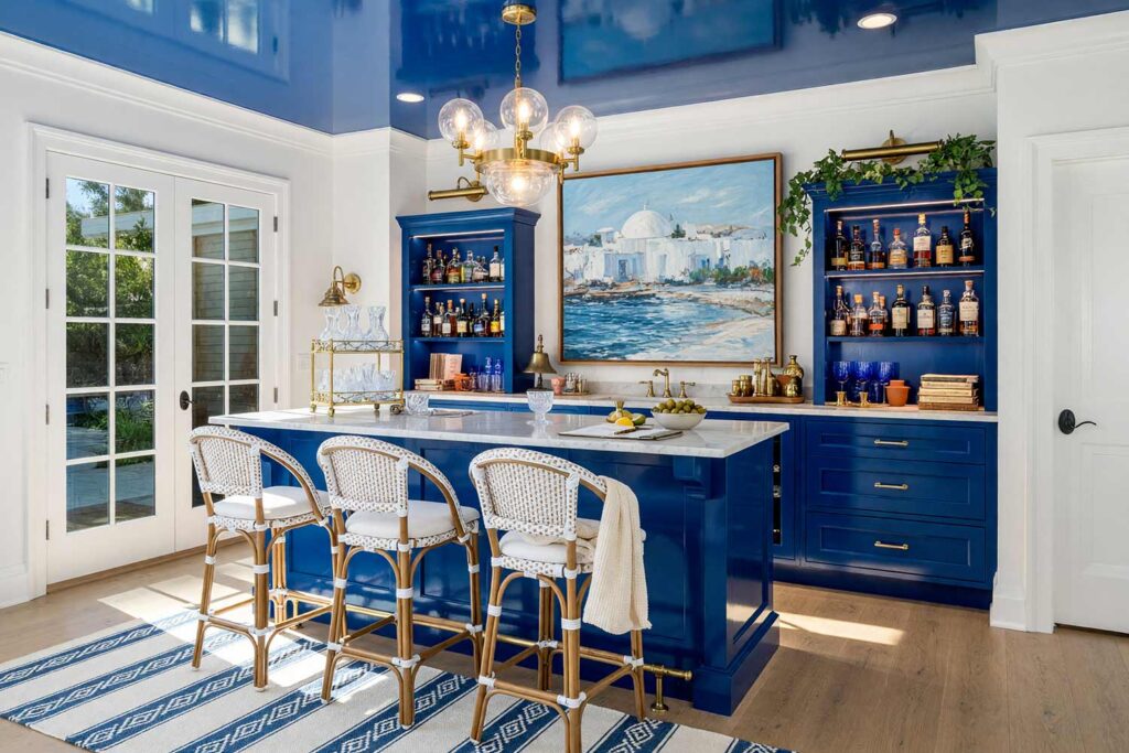 Home Bar in Cobalt Blue with Crisp White Walls and Cobalt Blue Ceiling-4, coastal boutique home bar crisp white walls cobalt blue cabinetry ceiling high gloss interior paint bleached oak floors. A vibrant coastal boutique home bar in a Scottsdale neighborhood pairing airy crisp white walls with a high-gloss cobalt blue ceiling and matching wet bar cabinetry over bleached oak planks. Styled with woven rattan barstools, hand-blown glassware, brass nautical lighting, and an impressionist Greek island painting. Dynamic high-contrast illumination casts deep shadows and specular gloss reflections across the painted surfaces, evoking a sun-drenched Mediterranean resort.