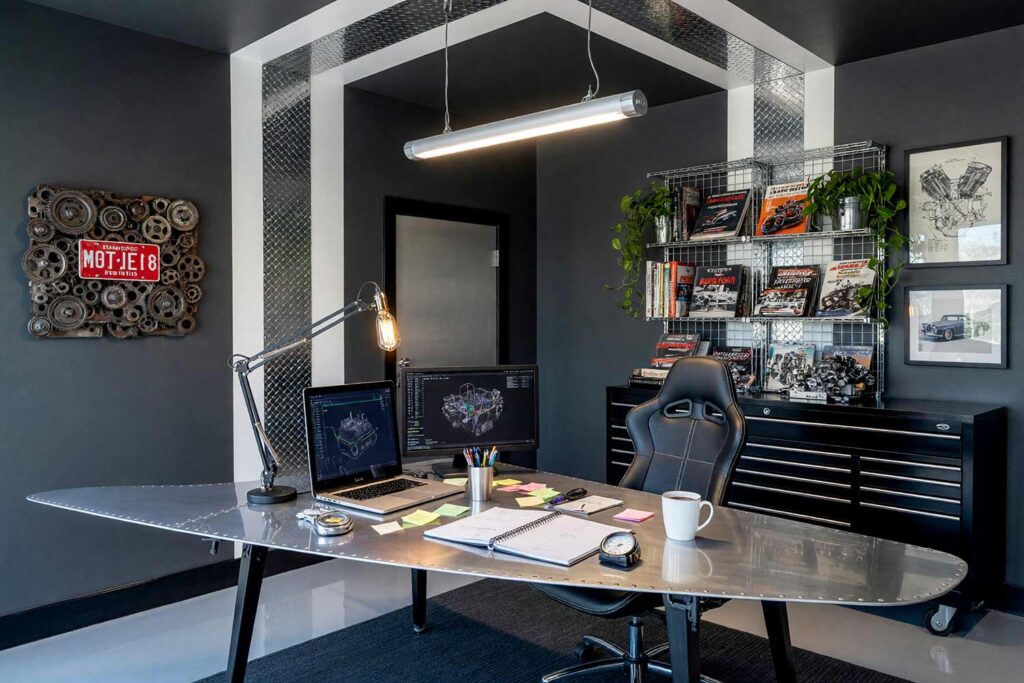Industrial Home Office with Gray Walls and Buffed Diamond-Plate Aluminum-1, industrial loft home office asphalt gray walls polar white racing bands diamond-plate aluminum jet black baseboards epoxy floors painting creative wall treatments. A high-performance automotive workspace in a Scottsdale neighborhood featuring a riveted aluminum wing desk with a powered-on laptop and scattered notes, an ergonomic bucket chair, and diamond-plate racing stripes. Midday sunlight beams across the epoxy floor, throwing sharp geometric shadows that elevate the shiny jet black trim and paddock-inspired design. painted accent wall with metal, dimensional accent wall, architectural accent wall, painted mural wall with metal accents, unique accent wall ideas, textured painted walls