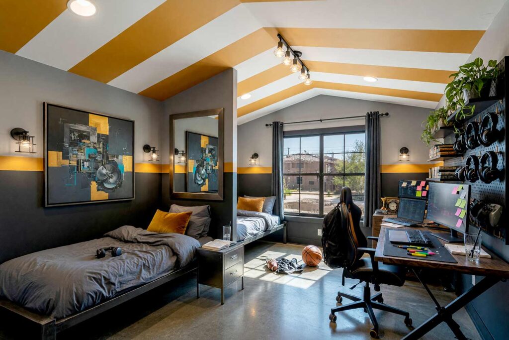 Industrial Loft Gaming Den Child’s Bedroom with Dark Gray and Yellow Accents-4, kid’s bedroom paint colors industrial loft soft fog gray charcoal gray golden amber soft white concrete floor. A modern industrial-inspired child’s gaming den in a Scottsdale neighborhood featuring soft fog gray walls, a split-level wall band in charcoal gray and golden amber, and lustrous soft white semi-gloss woodwork. The aspirational room combines an unmade blackened steel bed with a comprehensive study and gaming hub featuring a powered-on laptop, an ultrawide monitor, and a floor-to-ceiling pegboard organizing headsets and gear. Polished concrete floors and dramatic directional sunlight create a dynamic, inspiring setting engineered for focused homework and high-energy play. kid's bedroom paint colors, kids room color scheme, children's bedroom colors, kids bedroom color ideas, children's room paint colors