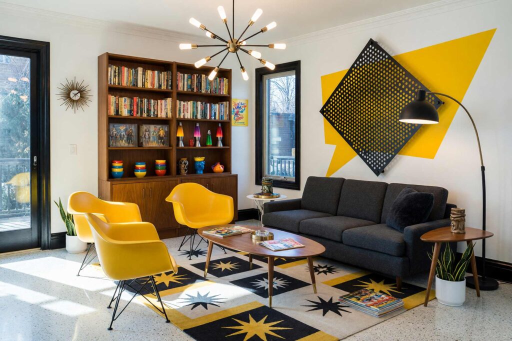 Living Room with Canary Yellow Speech-Balloon Burst Halftone and Perforated Aluminum Accent Wall-1, mid-century kitsch living room paper white walls primary canary accent wall halftone perforated aluminum signal black baseboards polished terrazzo floors painting creative wall treatments. A playful retro retreat in a Scottsdale neighborhood featuring a charcoal sectional sofa, a sputnik chandelier, packed mid-century bookshelves with action figures, and a dynamic atomic starburst area rug. The space is energized by an oversized yellow speech-balloon burst and a perforated aluminum accent panel casting intricate shadow patterns. Strong sunlight streams through large glass doors, highlighting the glossy signal black trim and the vibrant comic-book aesthetic. painting creative wall treatments, creative wall treatments, mixed material wall treatments, dimensional painted walls, textured accent wall ideas, metal accent wall ideas