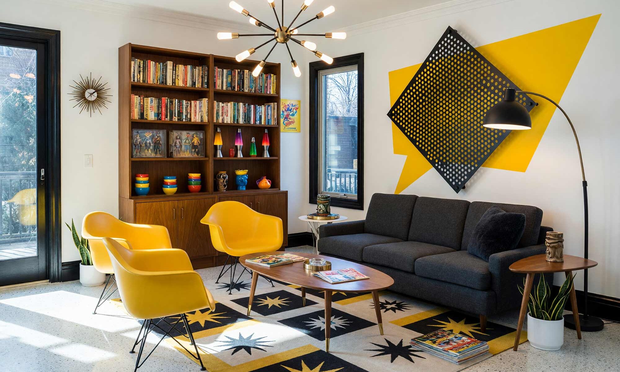 Living Room with Canary Yellow Speech-Balloon Burst Halftone and Perforated Aluminum Accent Wall-1, mid-century kitsch living room paper white walls primary canary accent wall halftone perforated aluminum signal black baseboards polished terrazzo floors painting creative wall treatments. A playful retro retreat in a Scottsdale neighborhood featuring a charcoal sectional sofa, a sputnik chandelier, packed mid-century bookshelves with action figures, and a dynamic atomic starburst area rug. The space is energized by an oversized yellow speech-balloon burst and a perforated aluminum accent panel casting intricate shadow patterns. Strong sunlight streams through large glass doors, highlighting the glossy signal black trim and the vibrant comic-book aesthetic. painting creative wall treatments, creative wall treatments, mixed material wall treatments, dimensional painted walls, textured accent wall ideas, metal accent wall ideas