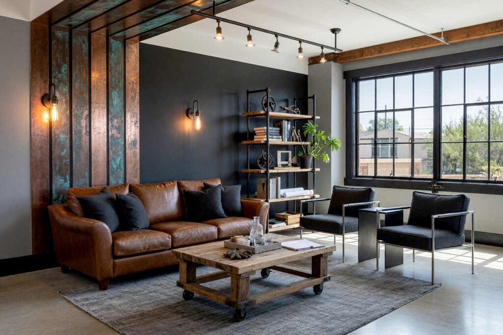 Phoenix Industrial Loft Living Room with Gray Walls and Patina Copper Strips-4, industrial loft living room ash gray walls graphite charcoal accent wall patinated copper strips soot black baseboards concrete floors painting creative wall treatments. A bold industrial space in a Scottsdale neighborhood featuring a cognac leather sofa, poured-concrete floors, blackened-steel sconces with Edison bulbs, and an accent wall of graphite charcoal with verdigris patinated copper strips. Natural sunlight pours through factory windows, highlighting the shiny soot black trim and architectural textures. painting creative wall treatments, creative wall treatments, mixed material wall treatments, dimensional painted walls, textured accent wall ideas, metal accent wall ideas