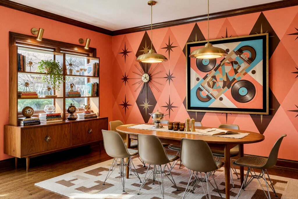 Retro Atomic Dining Room with Coral Walls and Espresso Brown Starbursts-6, retro atomic dining room coral walls espresso brown painted wall graphics soft white ceiling honey oak flooring. An entertaining space in a Scottsdale neighborhood featuring vibrant coral walls, a soft white ceiling, and an espresso brown starburst and harlequin diamond painted wall graphic. Detailed with a teak dining table, molded fiberglass chairs, dense open shelving, and honey oak floors. Intense directional daylight creates sharp, dramatic shadows, establishing an unforgettable mid-century vibe. hand-painted wall designs, decorative wall painting