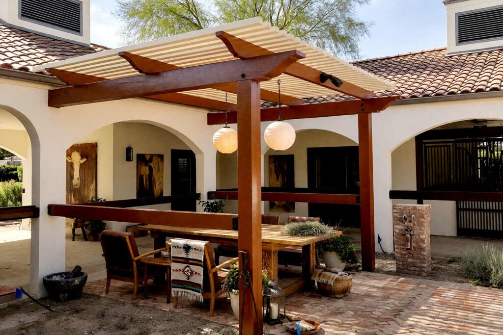 Southwestern Hacienda Pergola with Terracotta Posts and Warm Bone Slats-4, southwestern hacienda pergola deep clay timber warm bone slats trellis pergola paint colors. Situated in an upscale Scottsdale neighborhood, this Southwestern pergola pairs semi-gloss deep clay posts and trellis work with luminous warm bone roof slats. Saltillo tiles, equipale chairs, potted cacti, and glowing paper lanterns create a grounded hacienda escape under dramatic golden-hour shadows. painting a cedar pergola, ramada paint colors, trellis paint colors, backyard shade structure colors, best paint for an outdoor pergola
