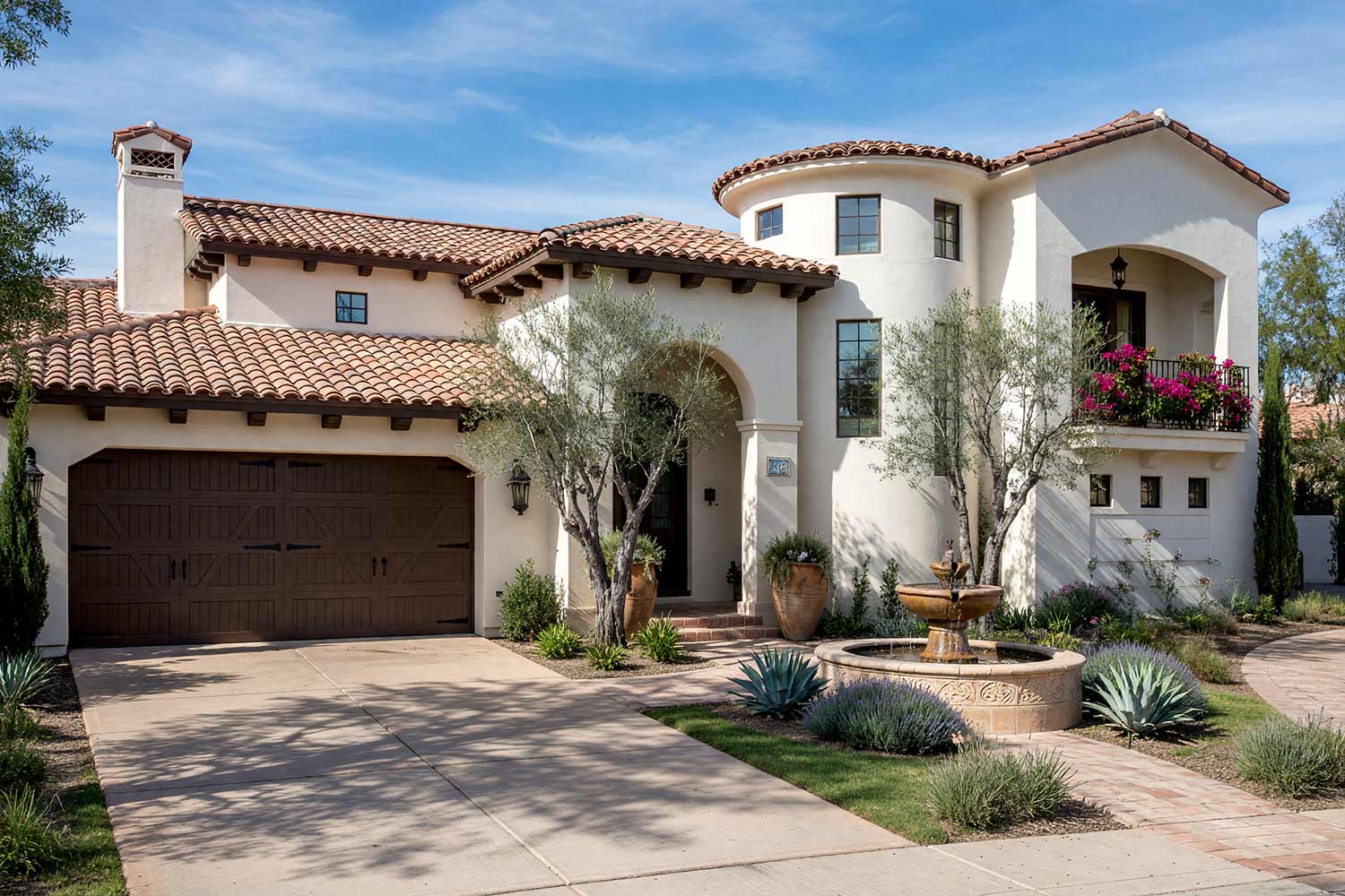 Spanish Revival Arcadia Home with Creamy Stucco and Espresso Brown Trim-6, spanish revival exterior paint colors creamy bone stucco espresso brown door soot black lanterns flagstone walkway front facade. A custom estate in a Scottsdale neighborhood featuring freshly painted stucco, glossy hand-finished trim, and elevated exterior painting curb appeal. Hand-thrown terracotta urns spilling trailing rosemary flank an arched entry set against rich sun-faded terracotta barrel tiles. A tiered Cantera stone fountain bubbles gently while dramatic dusk lighting casts deep shadows and illuminates soot black iron lanterns. spanish revival exterior paint colors, spanish style house paint colors, santa barbara exterior colors, modern mediterranean house paint, spanish colonial revival exterior colors