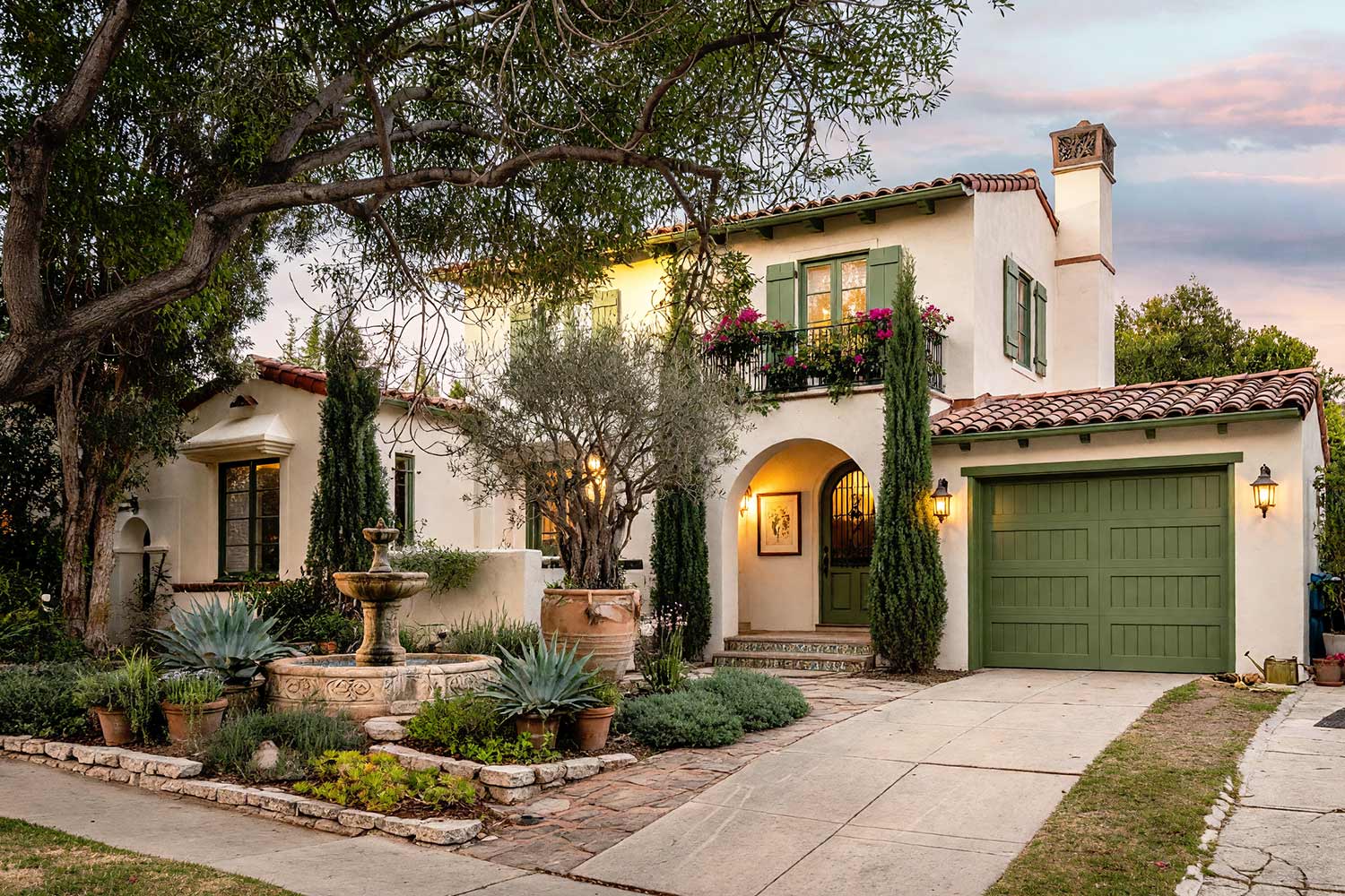 Spanish Revival Exterior with Alabaster Walls and Olive Moss Accents-5, spanish revival exterior paint colors gentle alabaster stucco olive moss shutters coal black balcony limestone walkway front facade. A custom estate in a Scottsdale neighborhood featuring freshly painted stucco, glossy hand-finished trim, and elevated exterior painting curb appeal. Semi-gloss olive moss shutters and an arched timber door pair with delicate coal black balcony rails and baked terracotta roof tiles. A carved Cantera stone fountain trickles softly amid potted olive trees, creeping thyme, and lush desert landscaping beneath dynamic late-afternoon sunlight. spanish revival exterior paint colors, spanish style house paint colors, santa barbara exterior colors, modern mediterranean house paint, spanish colonial revival exterior colors