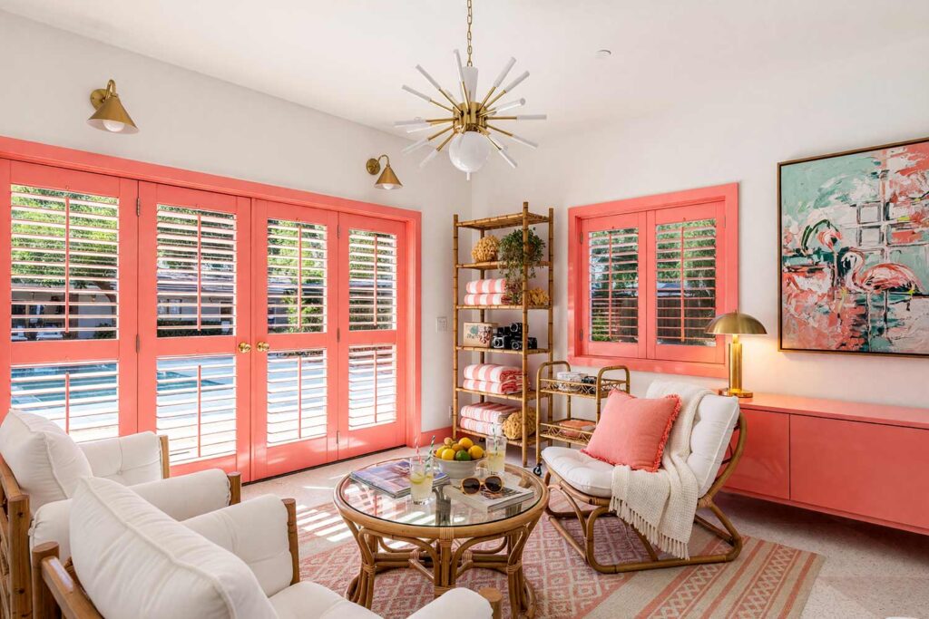 Sun Room with White Walls and High-Gloss Coral Pink Trim-2, palm springs poolside sun room chalk white walls coral pink louvered doors trim high gloss interior paint terrazzo floors. An airy Palm Springs-inspired poolside sun room in a Scottsdale neighborhood featuring chalk white walls and ceiling accented by high-gloss coral pink louvered doors and shiny trim. Outfitted with vintage rattan lounge chairs, leafy potted palms, cabana-striped towels, and an atomic starburst chandelier over terrazzo tile. Piercing desert sunlight casts dramatic high-contrast linear shadows across the reflective surfaces, evoking a permanent poolside vacation.