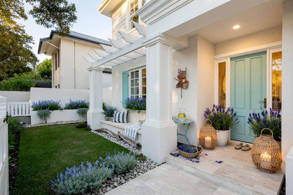 Entry Courtyard with Creamy Off-White Walls White Trim and Dusty Turquoise Door-4, coastal hamptons exterior courtyard paint colors creamy off-white walls sandstone white trim dusty turquoise door. This Scottsdale courtyard pairs matte creamy off-white stucco with a semi-gloss dusty turquoise door and cloud white planters. Staged with woven rattan lanterns, blooming hydrangeas, and striped cushions under dramatic late-afternoon golden hour light. exterior courtyard paint colors, painting outdoor courtyard, enclosed courtyard color schemes, front courtyard painting ideas, front courtyard color ideas, courtyard wall paint colors
