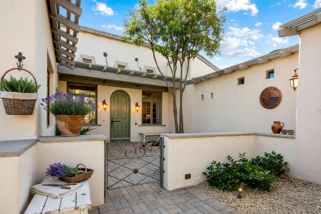 French Country Courtyard with Off-White Walls and Dove Gray Trim and Olive Green Door-5, french country exterior courtyard paint colors creamy off-white plaster dove gray trim olive green door. This custom Scottsdale entry sanctuary pairs matte creamy off-white plaster walls with semi-gloss olive green millwork and dove gray trim. Complemented by a distressed white planter bench, potted lavender, and dramatic late-afternoon golden hour shadows. exterior courtyard paint colors, painting outdoor courtyard, enclosed courtyard color schemes, front courtyard painting ideas, front courtyard color ideas, courtyard wall paint colors