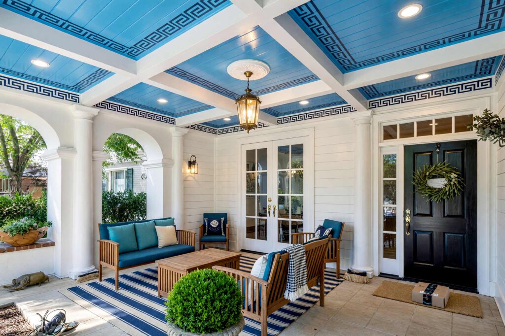 Mediterranean Porch Ceiling in Light Blue and Navy with Greek Key Pattern-6-FEATURE, neoclassical porch ceiling ideas robins egg blue navy greek key border bright white columns black door. This custom Scottsdale residence showcases a semi-gloss robin's egg blue ceiling with a navy Greek key border framed by bright white columns and matte soft white siding. Black lantern sconces, carved stone boxwood urns, and a black door provide formal symmetry. Dynamic golden hour lighting sculpts deep shadows across the millwork. porch ceiling paint ideas, patio ceiling color ideas, painted patio ceiling, striped porch ceiling, black porch ceiling, exterior ceiling paint colors, Southern porch ceiling colors, desert porch ceiling colors