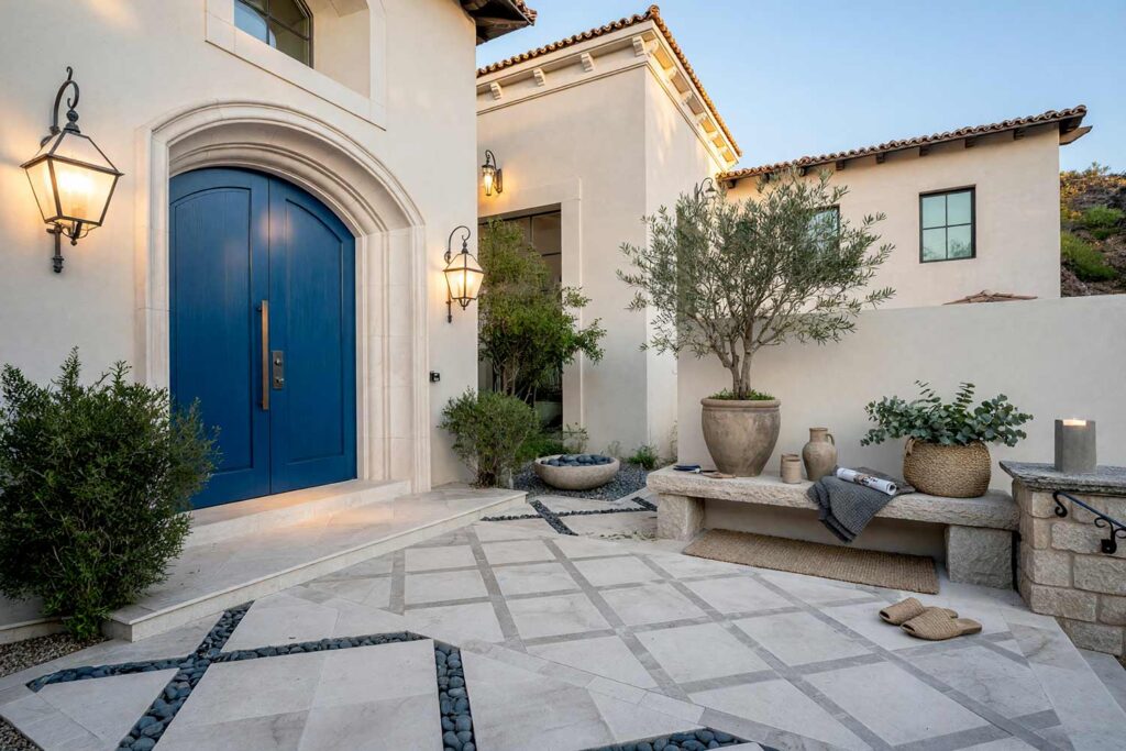 Modern Organic Courtyard with Cream Walls and White Trim and Cobalt Blue Door-2, modern organic exterior courtyard paint colors pale stone walls soft white trim cobalt blue entry door. This custom Scottsdale entry sanctuary pairs uniform matte pale stone painted walls with a semi-gloss cobalt blue door and soft white trim. Staged with large-format running bond pavers, black basalt joints, an olive urn, and high-contrast late-afternoon golden hour shadows. entry courtyard paint colors, courtyard stucco paint colors, courtyard door color ideas, walled courtyard color schemes, outdoor courtyard color palette