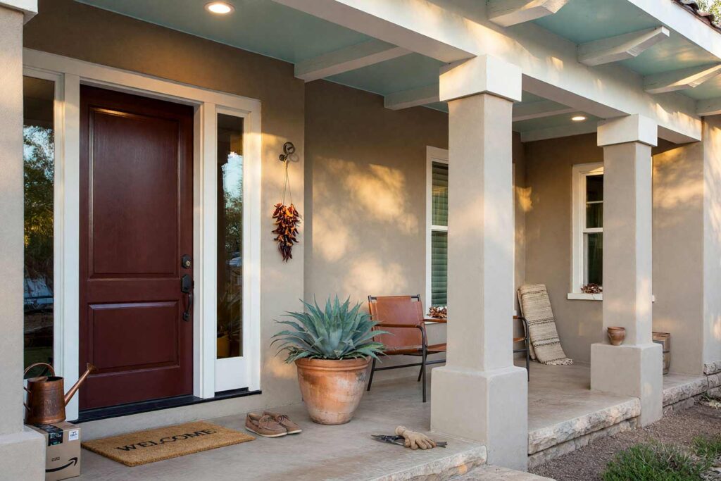 Porch Ceiling with Pale Watery Aqua Ceiling and Warm White Fascia and Burgundy Door-8, covered patio ceiling paint pale watery aqua arizona ranch revival greige stucco burgundy door. Designed for a custom home in a Scottsdale neighborhood, this ranch veranda pairs a shiny semi-gloss pale watery aqua ceiling with matte greige stucco. Warm white fascia, a rich burgundy front door, leather sling chairs, and potted agave complete the desert aesthetic. Dynamic late-afternoon lighting creates deep shadows and brilliant highlights across the woodwork. porch ceiling ideas, painted porch ceiling ideas, haint blue porch ceiling, front porch ceiling paint colors, covered patio ceiling paint, blue porch ceiling, haint blue paint colors