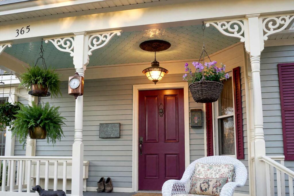 Victorian Porch with Pale Seafoam Scalloped Wood Shingles Ceiling and Plum Door-5, painted porch ceiling ideas pale seafoam scalloped wood shingles cream brackets dove gray siding plum door. Situated at an elegant Scottsdale residence, this Victorian veranda pairs a semi-gloss pale seafoam fish-scale shingle ceiling with cream gingerbread fretwork and matte dove gray siding. An etched brass lantern, wicker rocker, and plum door deliver classic painted lady curb appeal. Dynamic golden hour sunlight sculpts deep shadows and brilliant highlights across the woodwork. porch ceiling paint ideas, patio ceiling color ideas, painted patio ceiling, striped porch ceiling, black porch ceiling, exterior ceiling paint colors, Southern porch ceiling colors, desert porch ceiling colors